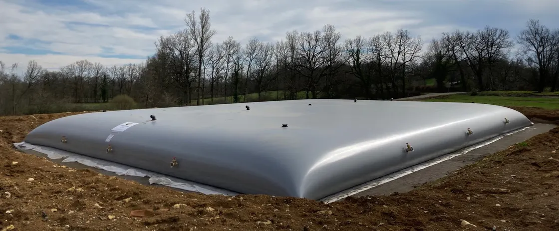 Cisterna flexible gris para digestato instalada sobre lámina de protección junto a un digestor de planta de biogás