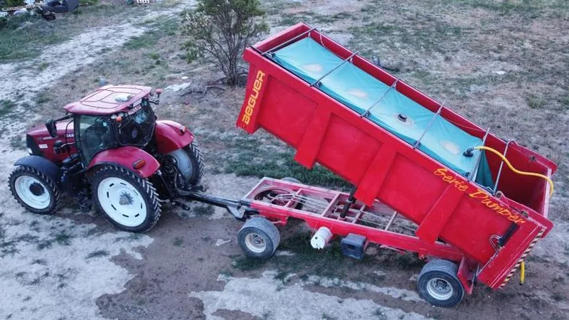 Depósito de abono líquido cinchado sobre un remolque basculante agrícola, remolcado por tractor