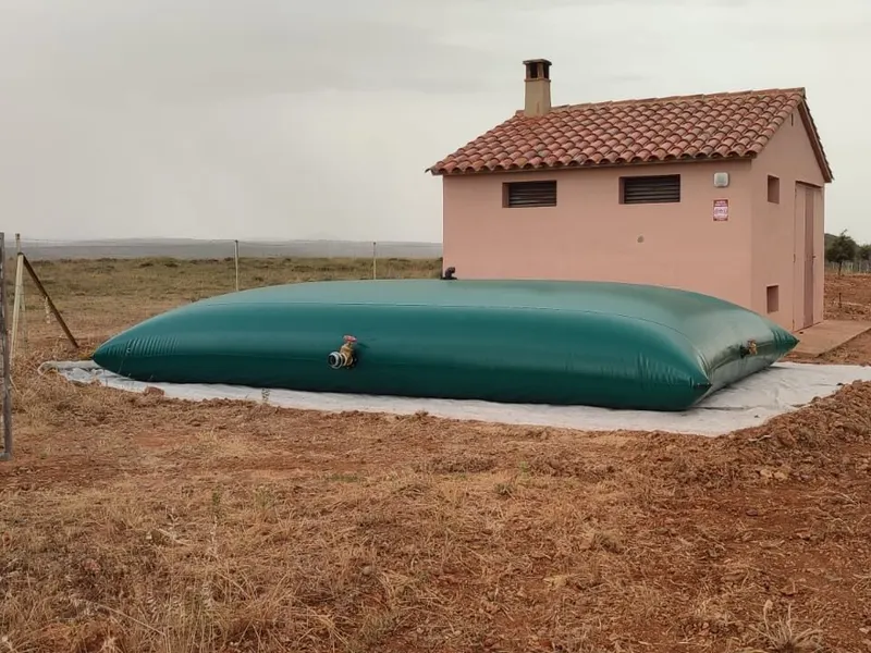 Depósito flexible para agua instalado sobre geotextil junto a una caseta en finca agrícola